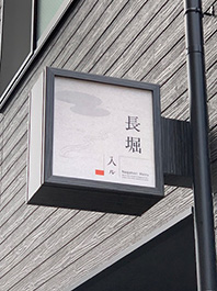 大阪市中央区の新築の外国人観光客向けの旅館の看板製作をさせて頂きました。
建物のイメージに合わせて看板本体は黒基調のダイノックシート貼り。
広告面は和紙調に照明は電球色のLEDにて製作しました。